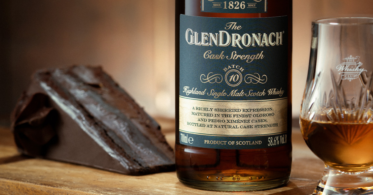 a bottle of Glendronach Cask Strength Highland single malt whisky alongside a cut crystal Glencairn glass and a wedge of cake.